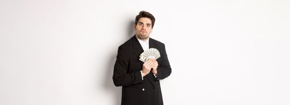 Image of greedy guy in black suit, holding money and unwilling to share, standing over white background.