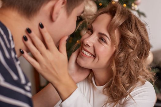 Happy loving couple relaxing on bed at home, young man touching smiling beautiful woman face, looking in the eyes enjoying togetherness and tenderness in love, close up view