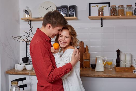 Happy young lovely couple on kitchen hugging each other. They enjoy spending time togehter. They show emotions to each other