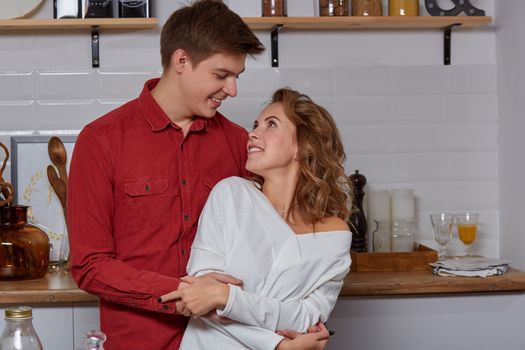 Happy young lovely couple on kitchen hugging each other. They enjoy spending time togehter. They show emotions to each other