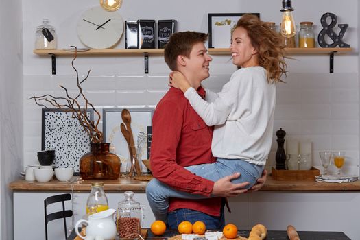 Happy young lovely couple on kitchen hugging each other. They enjoy spending time togehter. The man holding his girlfriend