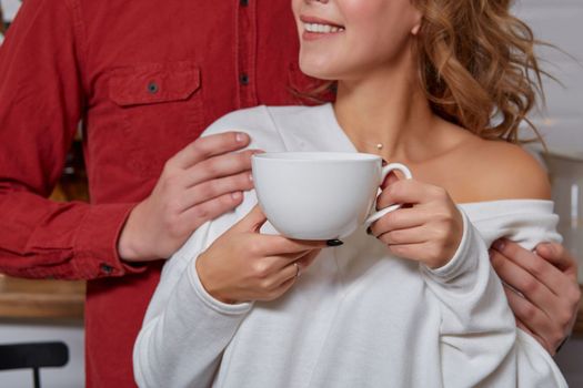 Happy young lovely couple on kitchen hugging each other. They enjoy spending time togehter. They drink coffee and smiling