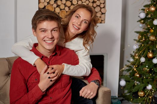 Happy young lovely couple on living room sitting on the couch near christmass tree enjoying each other