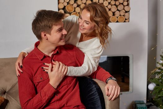 Happy young lovely couple on living room sitting on the couch near christmass tree enjoying each other