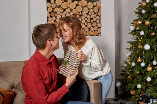 Happy young lovely couple on living room sitting on the couch near christmass tree enjoying each other