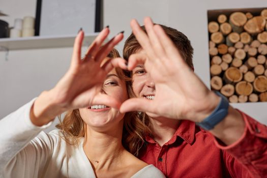 Close up portrait of a beautiful couple depicting the heart with their own hands, smiling and enjoying the life