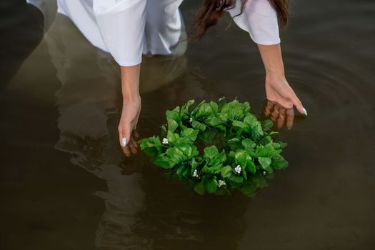 Close-up of woman in white dress in the water. Art with wreath in river. Wet witch Girl in the lake, mystical mysterious. Wreath in her hand, Slavic traditions and paganism