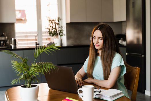 Cheerful young woman programmer works remotely on laptop and try to meet deadline at home. Candid girl with laptop is smiling and rejoices at successful work in IT company