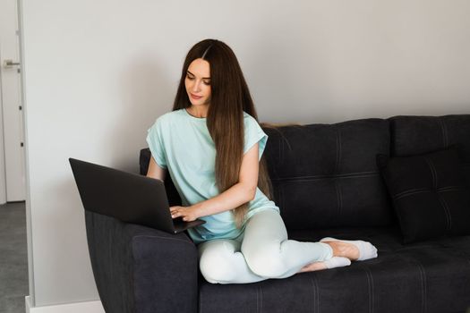 Cheerful young woman programmer works remotely on laptop and try to meet deadline at home. Candid girl with laptop is smiling and rejoices at successful work in IT company