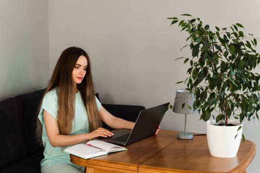 Cheerful young woman programmer works remotely on laptop and try to meet deadline at home. Candid girl with laptop is smiling and rejoices at successful work in IT company