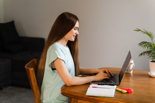 Cheerful girl with laptop typing text and chatting with friends and family in at home. Young woman have a break, watching online videos and trainings on laptop, preparing for conference