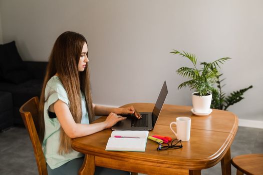 Cheerful girl with laptop typing text and chatting with friends and family in at home. Young woman have a break, watching online videos and trainings on laptop, preparing for conference