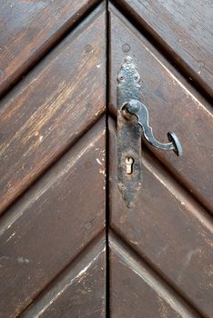 A locked double-leaf old entrance gate with hanging door handle. The wood is marked by the weather.