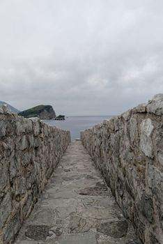 View along a castle keep protected with high stone walls to the Adriatic Sea. Dark thunderstorm clouds hang in the sky and disturb an oppressive calm.