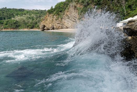 On a rock on the beach, a large wave breaks and creates a beautiful spray.