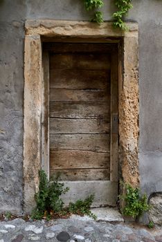 A very old locked entrance door with weathered wood in a European old town. The door frame is made of old sandstone and the facade has a crumbling plaster.