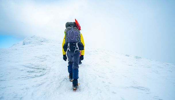 Man with large backpack walking to top of snowy winter mountain