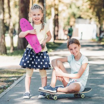 Beautiful little girls with skateboards looking at the camera and smiling in sunny day