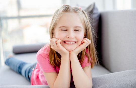 Smiling little girl lying on sofa in bright apartment