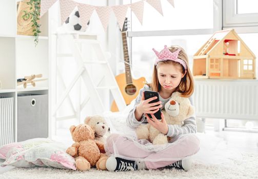Lovely little girl with toys and smartphone in children's room