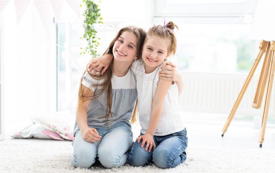 Happy sisters hugging sitting on floor in bright room