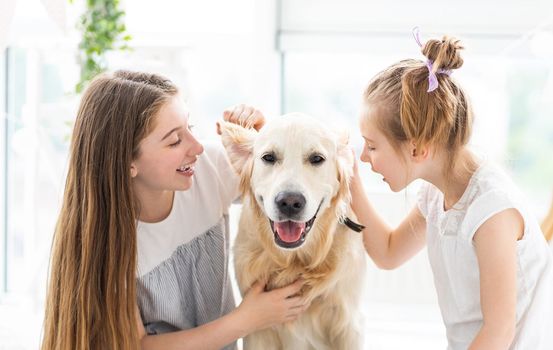 Cute girls whispering secrets into dog's ears indoors