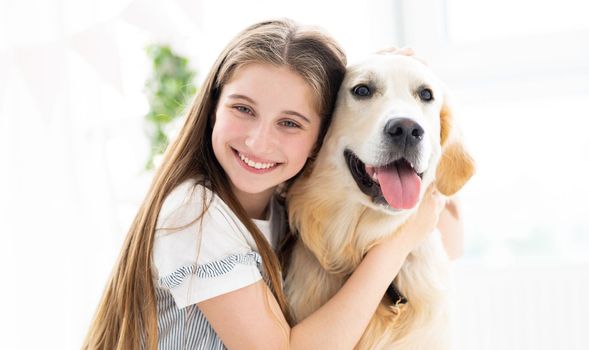Portrait of pretty teenage girl hugging beautiful dog indoors