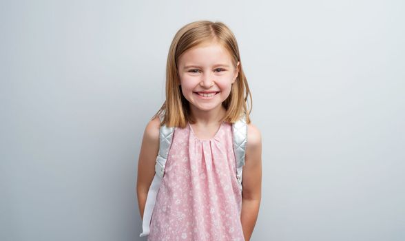 Schoolgirl with backpack posing on gray background