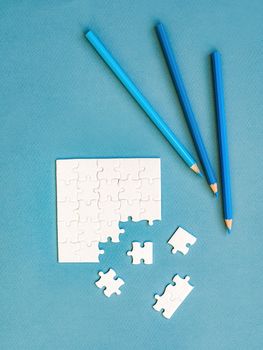 Small disassembled white square puzzle and pencils on a blue background