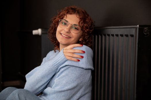 Satisfied girl. Warming up by the hot radiator. Efficient central heating at home. The winter period is the time for space heating.