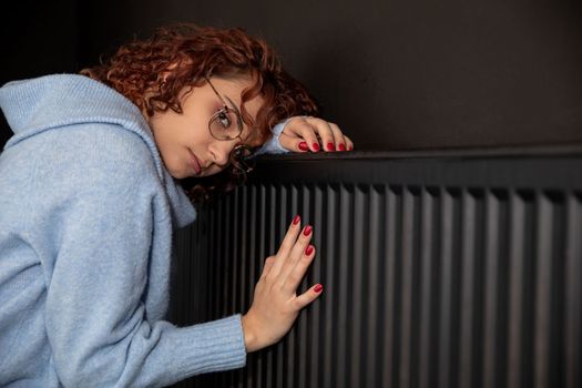 During the winter season and poor heating, the girl hugs the radiator. Central heating necessary in the house during the winter period.