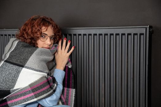 Hot radiator. A girl with curly hair and glasses warms herself at the heater. Central heating during initial startup.