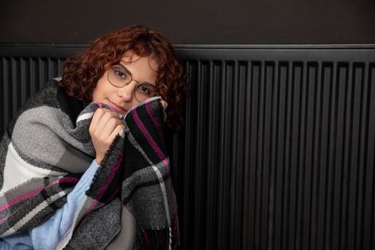A girl wrapped in a thick scarf. A faulty central heating system. A smiling 20-year-old girl warms herself by the heater.