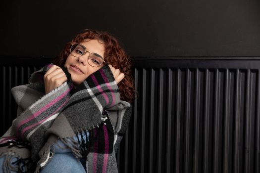 A girl wrapped in a thick scarf. A faulty central heating system. A smiling 20-year-old girl warms herself by the heater.