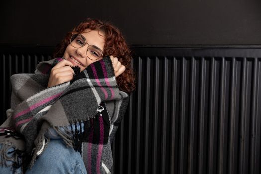 A girl wrapped in a thick scarf. A faulty central heating system. A smiling 20-year-old girl warms herself by the heater.