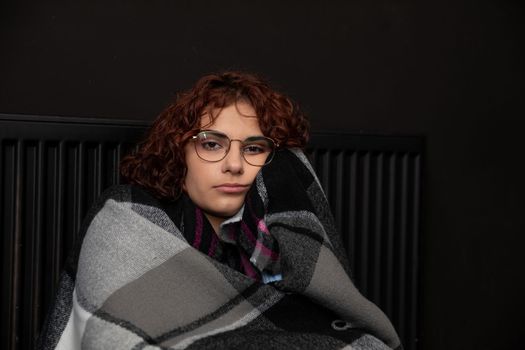 A girl sits wrapped in a scarf hoping the heater will finally start heating. Central heating during the first startup.