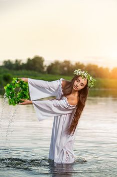 Beautiful black haired girl in white vintage dress and wreath of flowers standing in water of lake. Fairytale story. Warm art work. Sun flare