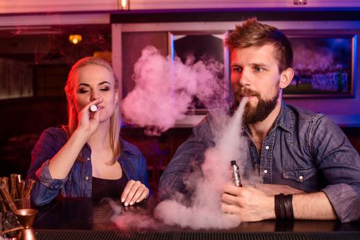 A man and woman smoking electronic cigarette in a vape bar. Vape shop