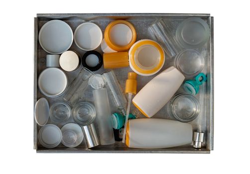 Used glass and plastic cosmetic container jars ready to recycle in stainless steel tray isolated on white background with clipping path. Recycle waste concept, Selective focus.