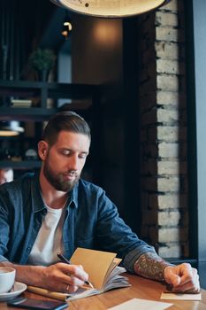 Man hand with pen writing on notebook on a wooden table. Man working at coffee shop