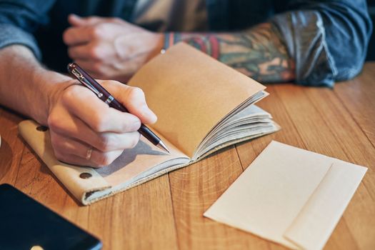 Man hand with pen writing on notebook on a wooden table. Man working at coffee shop. Close-up