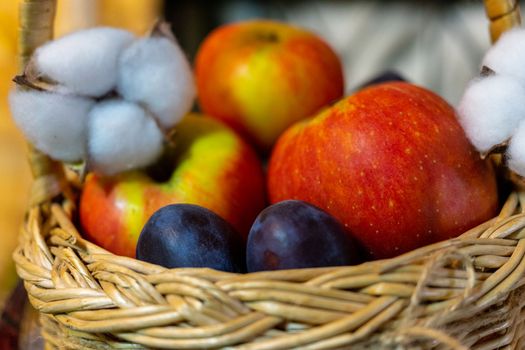 Ripe apples and plums in a vine basket close-up.