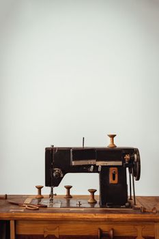 Old vintage sewing machine on wooden table on white wall background. Copy space, Selective focus.