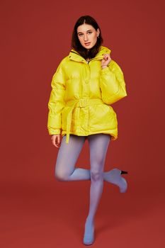 Image of young dark haired girl posing before camera in studio on red background. Fashion image of stylish woman wearing yellow jacket