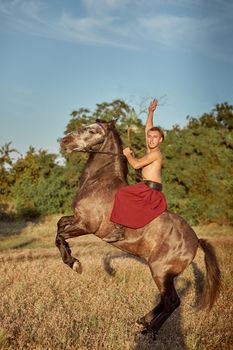 Handsome man cowboy riding on a horse - background of sky and trees. A man in red wide pants without a shirt. Show
