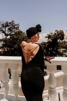 Stylish woman in the city. Fashion photo of a beautiful model in an elegant black dress posing against the backdrop of a building on a city street.