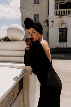 Stylish woman in the city. Fashion photo of a beautiful model in an elegant black dress posing against the backdrop of a building on a city street.