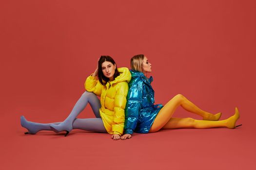 Two pretty girls in puffs posing for the camera in the studio. Blonde and brunette in stockings look confident in front of the camera, sit on floor back to back