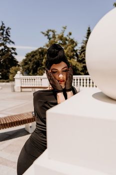 Stylish woman in the city. Fashion photo of a beautiful model in an elegant black dress posing against the backdrop of a building on a city street.