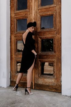 Stylish woman in the city. Fashion photo of a beautiful model in an elegant black dress posing against the backdrop of a building on a city street.